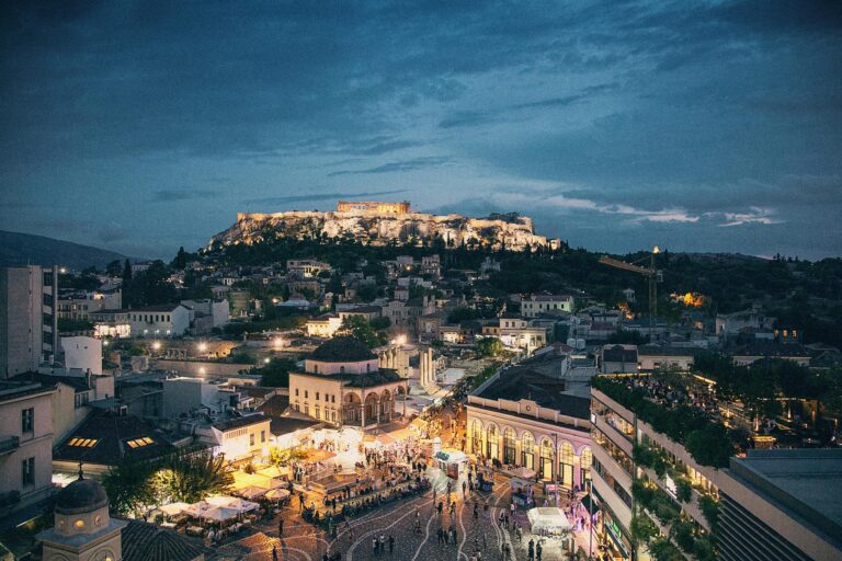 A vibrant night view of Athens with illuminated ancient ruins and modern city lights blending together.
