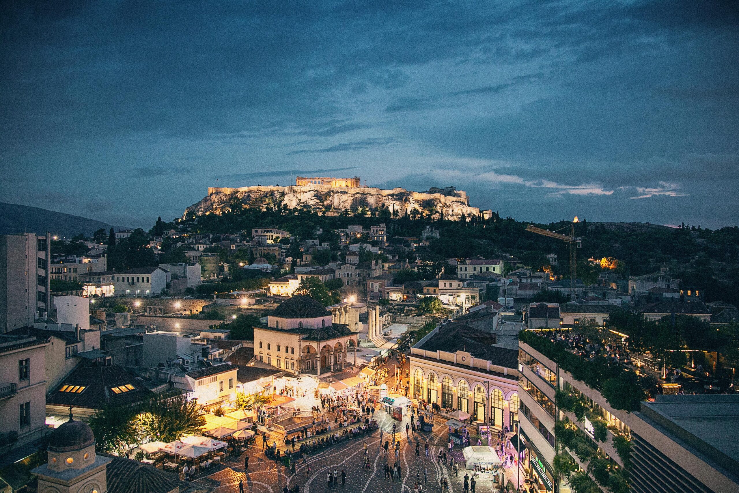A vibrant night view of Athens with illuminated ancient ruins and modern city lights blending together.