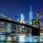 A breathtaking nighttime skyline of New York City, with the Brooklyn Bridge and towering skyscrapers illuminated against the dark sky.
