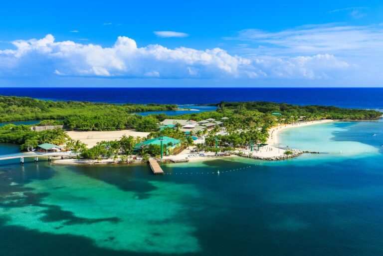 Aerial view of a tropical island resort with white sandy beaches, turquoise waters, and lush green vegetation. Roatan