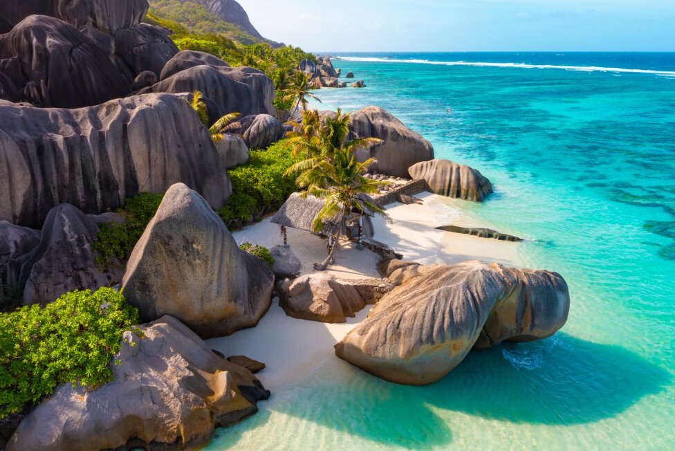 Seychelles : Stunning tropical beach with crystal-clear turquoise waters, lush palm trees, and dramatic granite boulders.