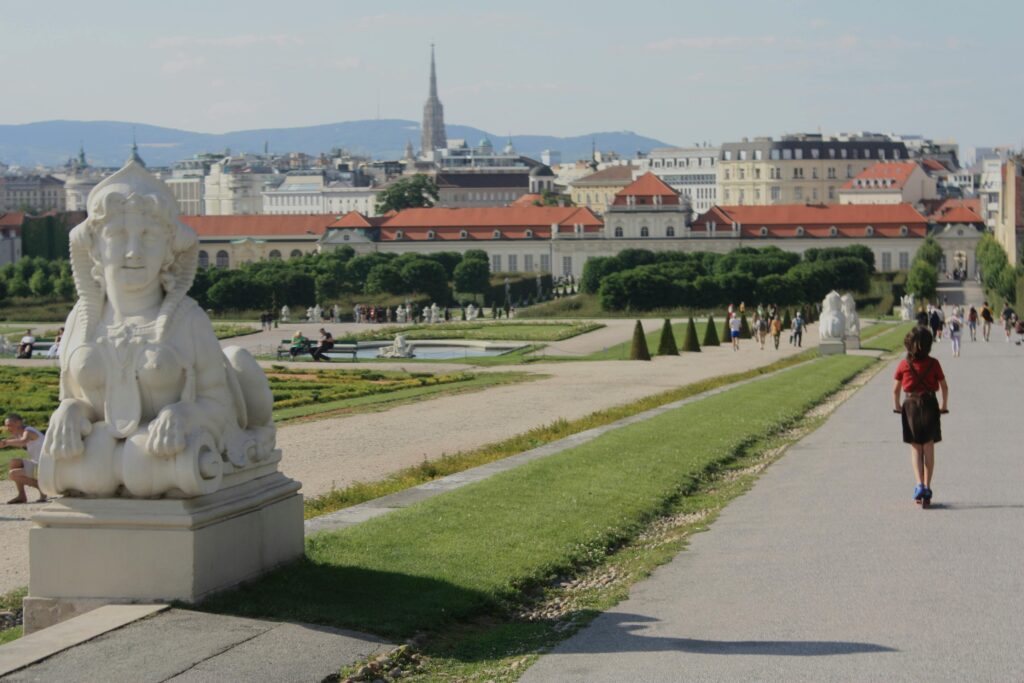 A picturesque cityscape featuring a Ferris wheel, historic architecture, and a river, with a clear blue sky in the background. vienna