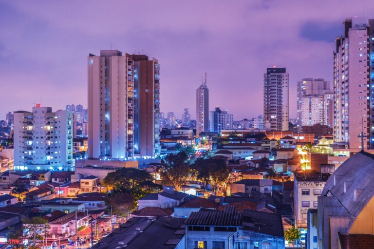 São Paulo ,A nighttime cityscape with a vibrant, densely packed skyline of illuminated high-rise buildings against a dramatic purple-blue sky.
